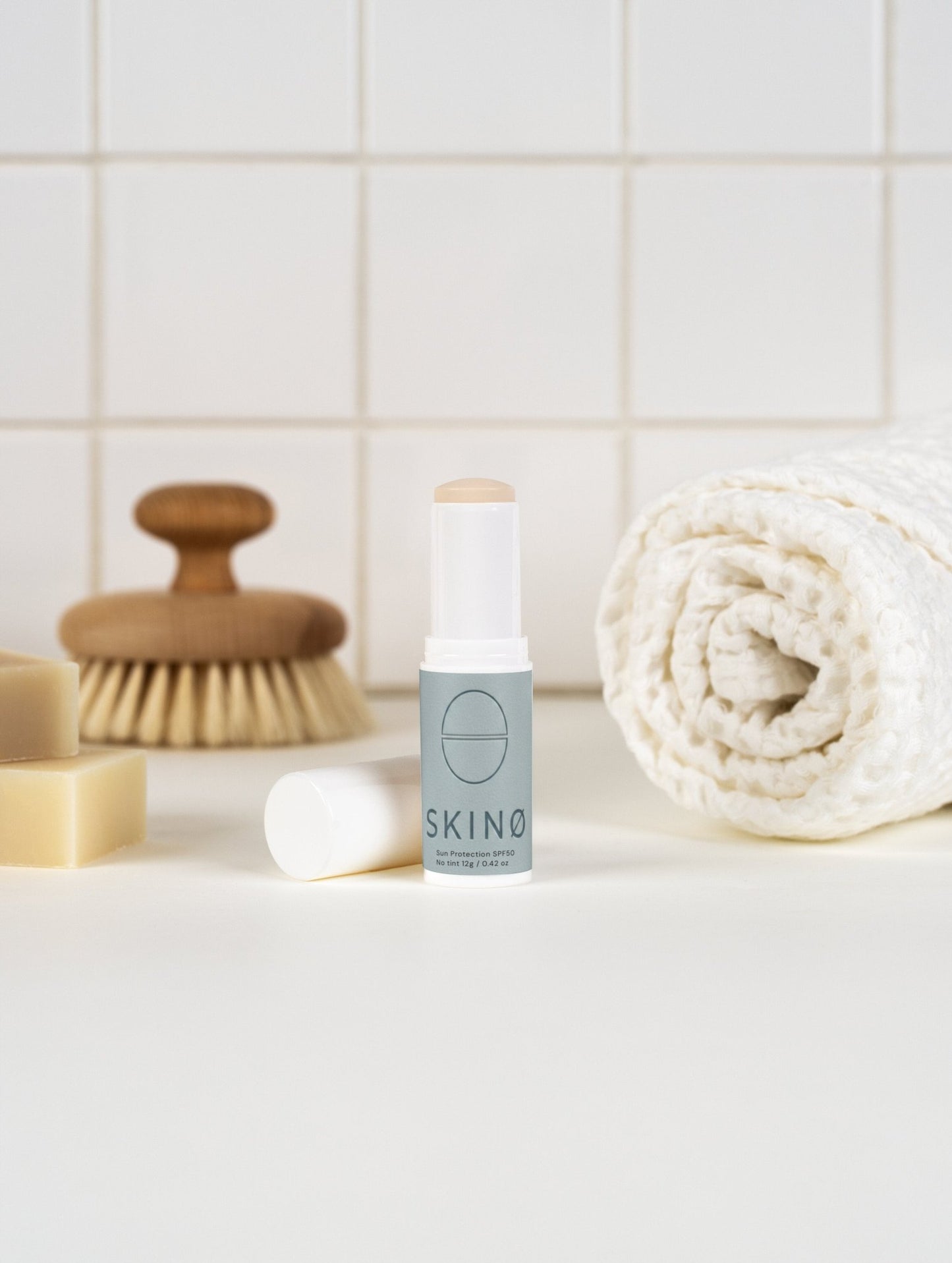 SKINØ Mineral Sun Stick SPF 50 lifestyle – mineral solskyddsstick
placerad i spa-inspirerad badrumsscen med naturliga badtillbehör,
representerar daglig hudvård rutiner med ekologisk, reef-safe
sunscreen för känslig och mogen hud, COSMOS ORGANIC certifierad
naturlig skincare.
