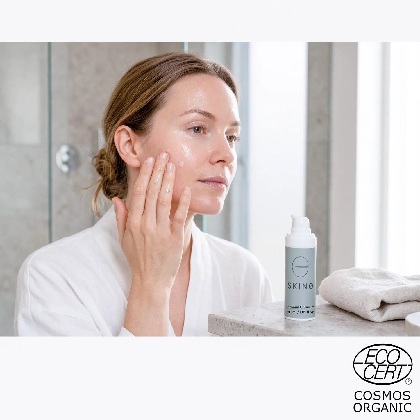 Kvinna applicerar SKINØ Nordic Glow Serum vitamin C serum i badrummet – morgonrutin för glow och jämnare hudton med vitamin C och hyaluronsyra, ECOCERT COSMOS ORGANIC.