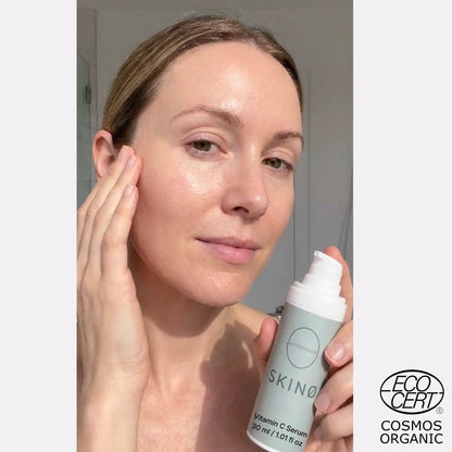 Kvinna håller SKINØ Nordic Glow Serum Vitamin C Serum 30ml mot ansiktet – naturlig glow och klar hud efter vitamin C serum, hyaluronsyra för återfuktning, ECOCERT COSMOS ORGANIC.